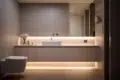 A modern bathroom featuring a sleek vanity with undermount lighting, a white sink, and a minimalistic design; a toilet is positioned alongside the vanity against gray walls.