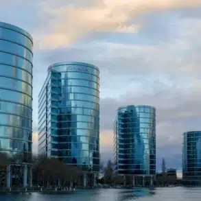 Five modern, curved glass office buildings reflecting the cloudy sky, situated along a waterfront with leafless trees nearby.
