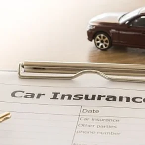A car insurance form lies on a table with a pen and a car key nearby. A small toy car rests on the form, symbolizing automobile coverage.