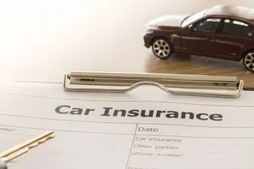 A car insurance form lies on a table with a pen and a car key nearby. A small toy car rests on the form, symbolizing automobile coverage.