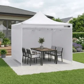 White canopy tent set up in a backyard with a dining table and chairs, surrounded by lush landscaping.