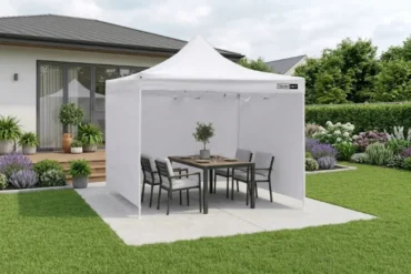 White canopy tent set up in a backyard with a dining table and chairs, surrounded by lush landscaping.
