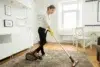 Woman vacuuming a plush rug in a brightly lit living room.