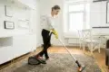 Woman vacuuming a plush rug in a brightly lit living room.
