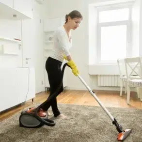 Woman vacuuming a plush rug in a brightly lit living room.