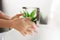 Person washing hands with soap under running water at a modern sink with a green plant in the background.