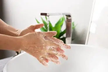 Person washing hands with soap under running water at a modern sink with a green plant in the background.