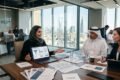 Business meeting with professionals reviewing recruitment analytics and resumes in a modern office overlooking Riyadh cityscape.