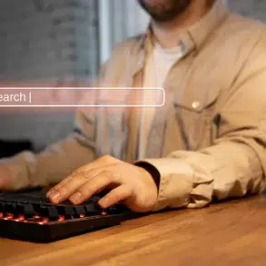 Man typing on a backlit keyboard with a search bar graphic overlaid.
