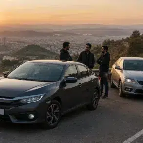 Three men stand beside a dark gray sedan and a silver sedan parked on a scenic mountain road at sunset.