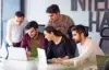 A group of five colleagues collaborate around laptops in a modern office. They appear focused and engaged, sharing ideas in a team discussion.