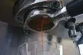 Fresh espresso pours from a coffee machine's portafilter into a clear glass below.
