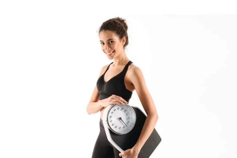 Woman in athletic wear smiling while holding a scale.