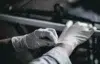 Person wearing white disposable gloves putting on the second glove in a dimly lit environment.