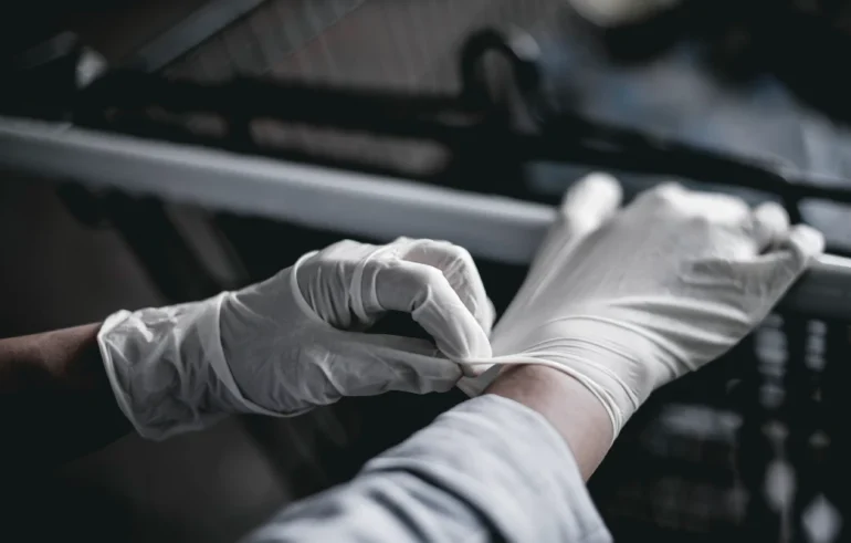 Person wearing white disposable gloves putting on the second glove in a dimly lit environment.