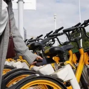A person stands next to a row of yellow rental bikes, holding a smartphone near a bike's QR code scanner. The scene conveys modern urban commuting.