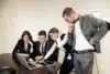 Four people in business attire are gathered around a laptop at a conference table, looking intently at the screen.