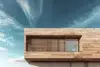 Modern wooden house facade with horizontal slats over a large window under a partly cloudy sky.