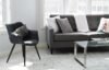 Modern living room with gray sofa, black chair, glass coffee table, and patterned cushions on a light rug near large windows.
