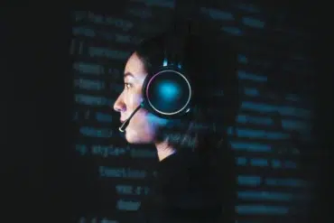 Profile view of a person wearing illuminated headphones with a microphone against a dark background filled with glowing blue code.