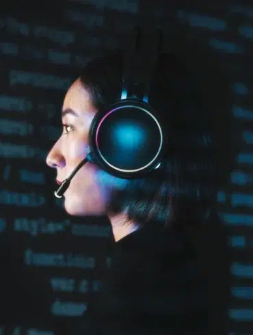 Profile view of a person wearing illuminated headphones with a microphone against a dark background filled with glowing blue code.