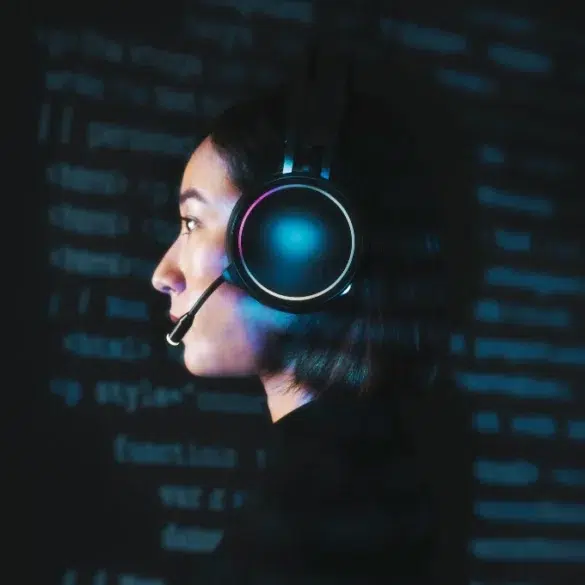 Profile view of a person wearing illuminated headphones with a microphone against a dark background filled with glowing blue code.