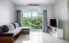Modern living room with a gray sectional sofa, TV stand, and large sliding glass doors opening to a balcony with lush green mountain views.