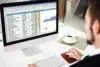 Person in suit works on a computer spreadsheet with charts, a coffee cup nearby.