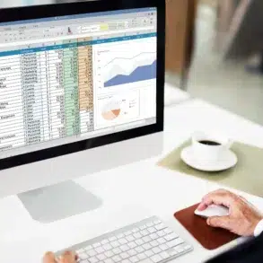 Person in suit works on a computer spreadsheet with charts, a coffee cup nearby.