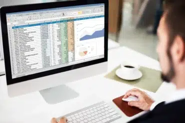 Person in suit works on a computer spreadsheet with charts, a coffee cup nearby.
