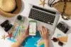 A person planning a trip with a laptop, smartphone with a map, paper maps, camera, hat, and sunglasses on a table. Mood is adventurous and organized.