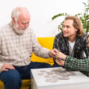 An elderly man, a younger man, and a boy are assembling a jigsaw puzzle at a white table.