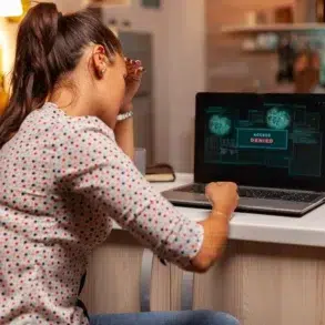 Frustrated woman holds her head while looking at a laptop screen displaying "ACCESS DENIED."
