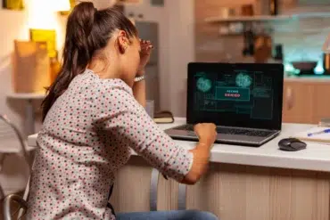 Frustrated woman holds her head while looking at a laptop screen displaying "ACCESS DENIED."