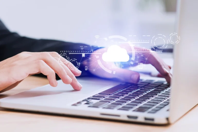 Close-up of hands typing on a laptop with a glowing cloud icon and network graphics overlayed.