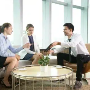Three business professionals in a modern office lounge discussing a tablet.