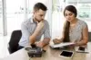 Man and woman discussing documents at a desk with a phone and tablet.