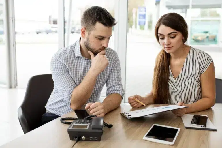 Man and woman discussing documents at a desk with a phone and tablet.