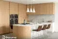 Modern kitchen with light wood cabinetry, double ovens, a marble backsplash, and a curved island with bar stools.
