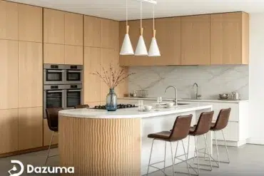 Modern kitchen with light wood cabinetry, double ovens, a marble backsplash, and a curved island with bar stools.