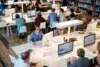 Diverse group of people working on computers in a library or study hall.