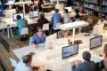 Diverse group of people working on computers in a library or study hall.