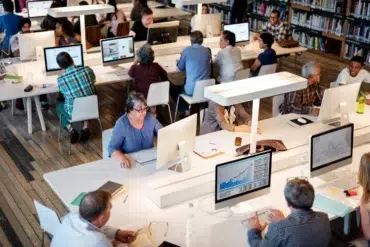 Diverse group of people working on computers in a library or study hall.