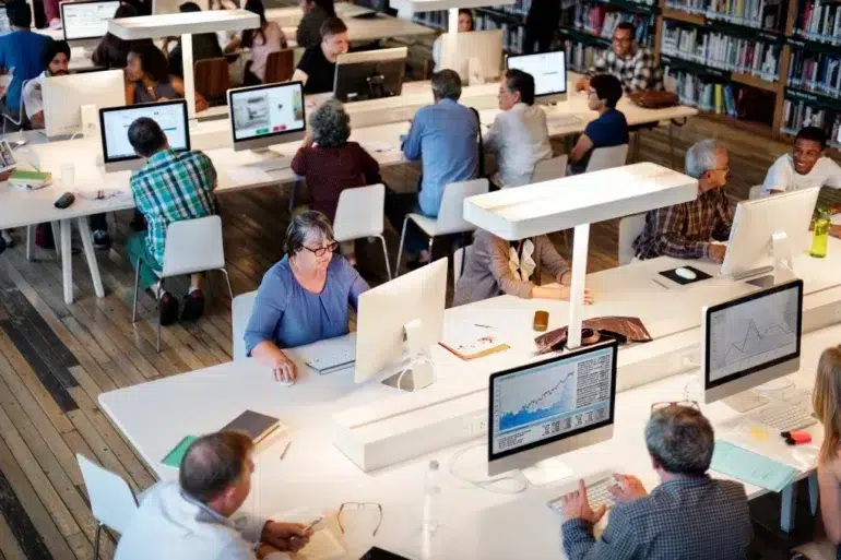 Diverse group of people working on computers in a library or study hall.