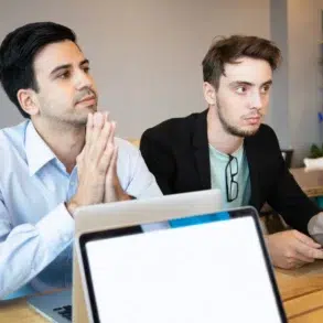 Two men in business attire at a table with laptops and a tablet.