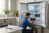 Technician testing refrigerator coils with a multimeter in a modern kitchen.