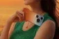 Woman in green top holding a Huawei smartphone with a tri-lens camera against her shoulder at sunset.