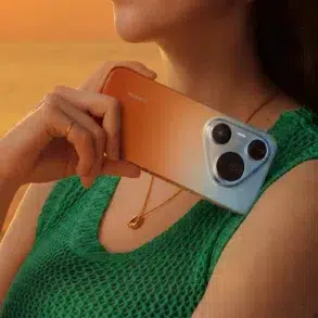 Woman in green top holding a Huawei smartphone with a tri-lens camera against her shoulder at sunset.