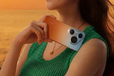 Woman in green top holding a Huawei smartphone with a tri-lens camera against her shoulder at sunset.