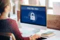 Woman at computer with screen displaying a large padlock icon and the word "PROTECTED".